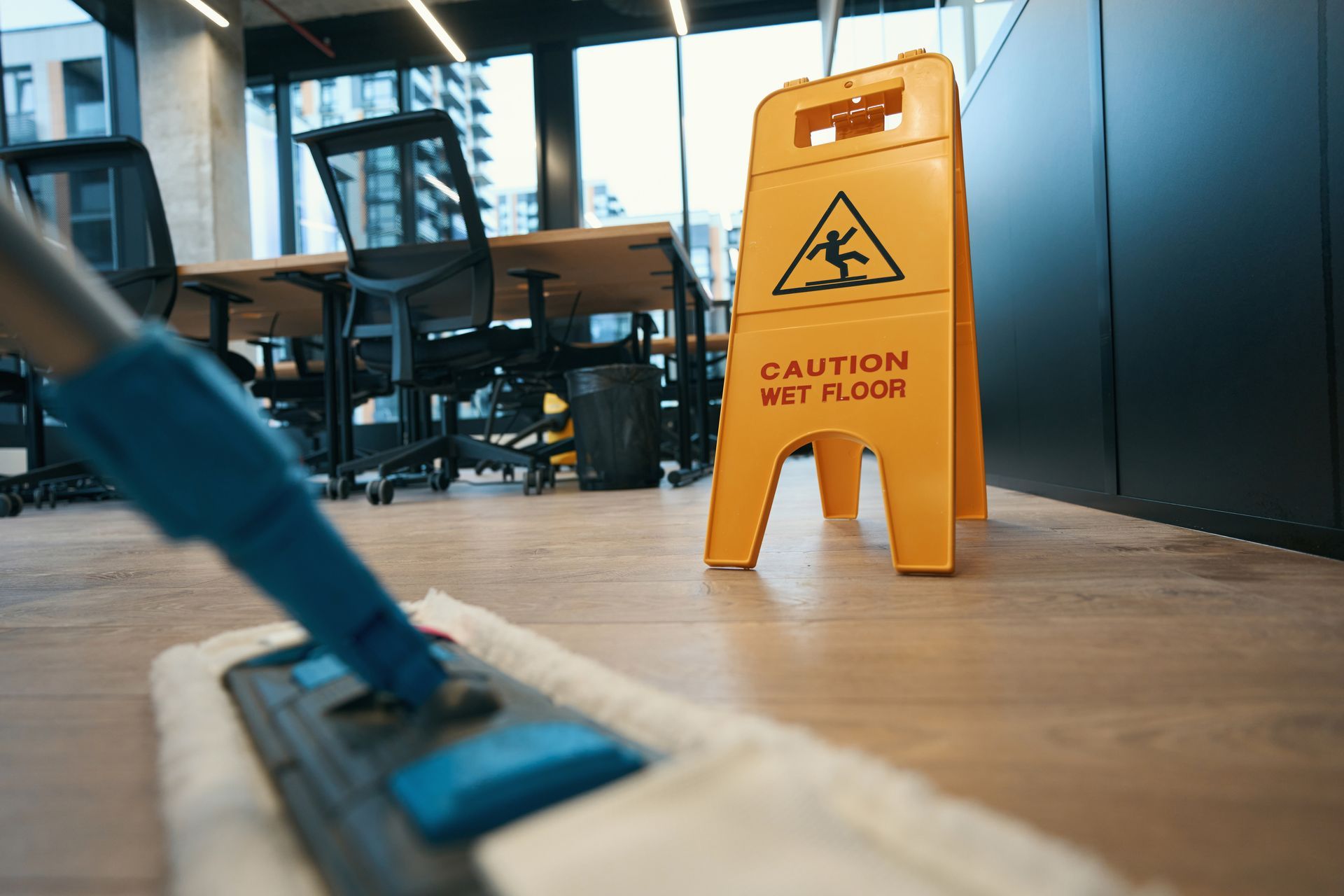 Yellow wet floor caution sign beside a mop in an office hallway