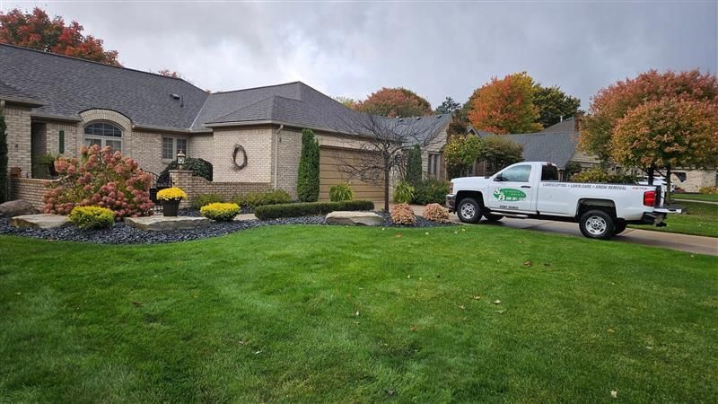 A white service truck parked in the driveway of a brick house with autumn-colored trees under a cloudy sky.