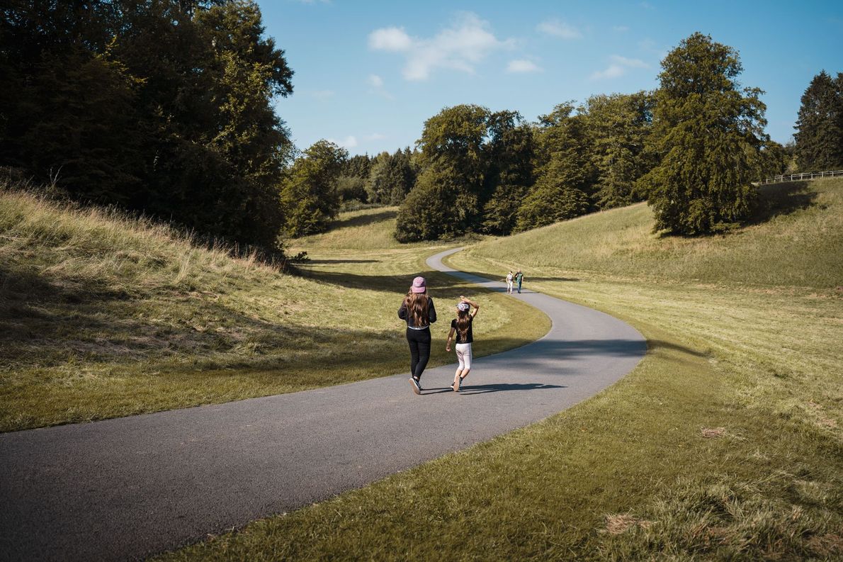 Two people jogging on a winding path through a grassy park under a sunny sky