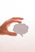 A hand is holding a paper speech bubble on a white background.