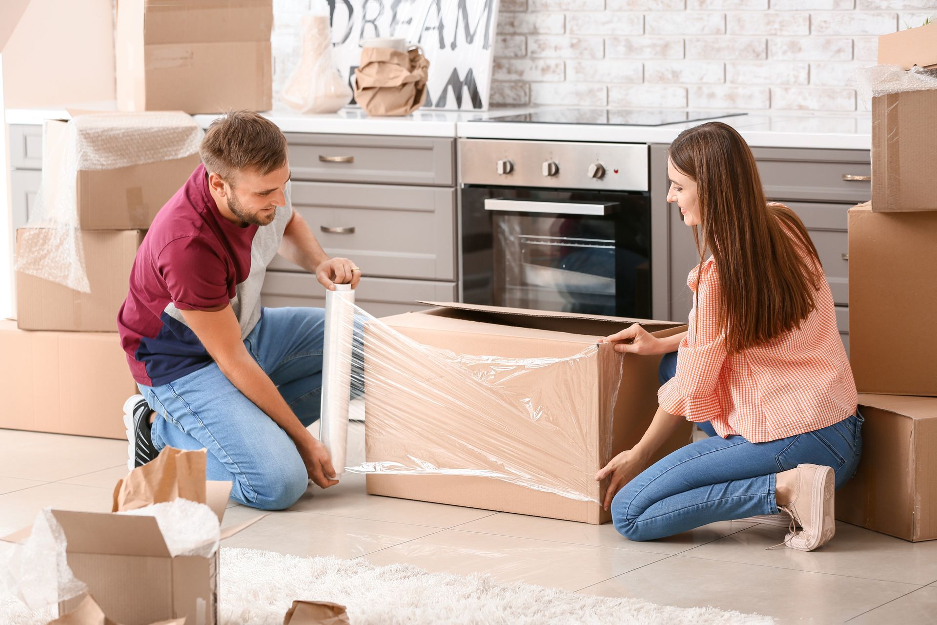 Couple packing a cardboard box with packing wrap in a kitchen.