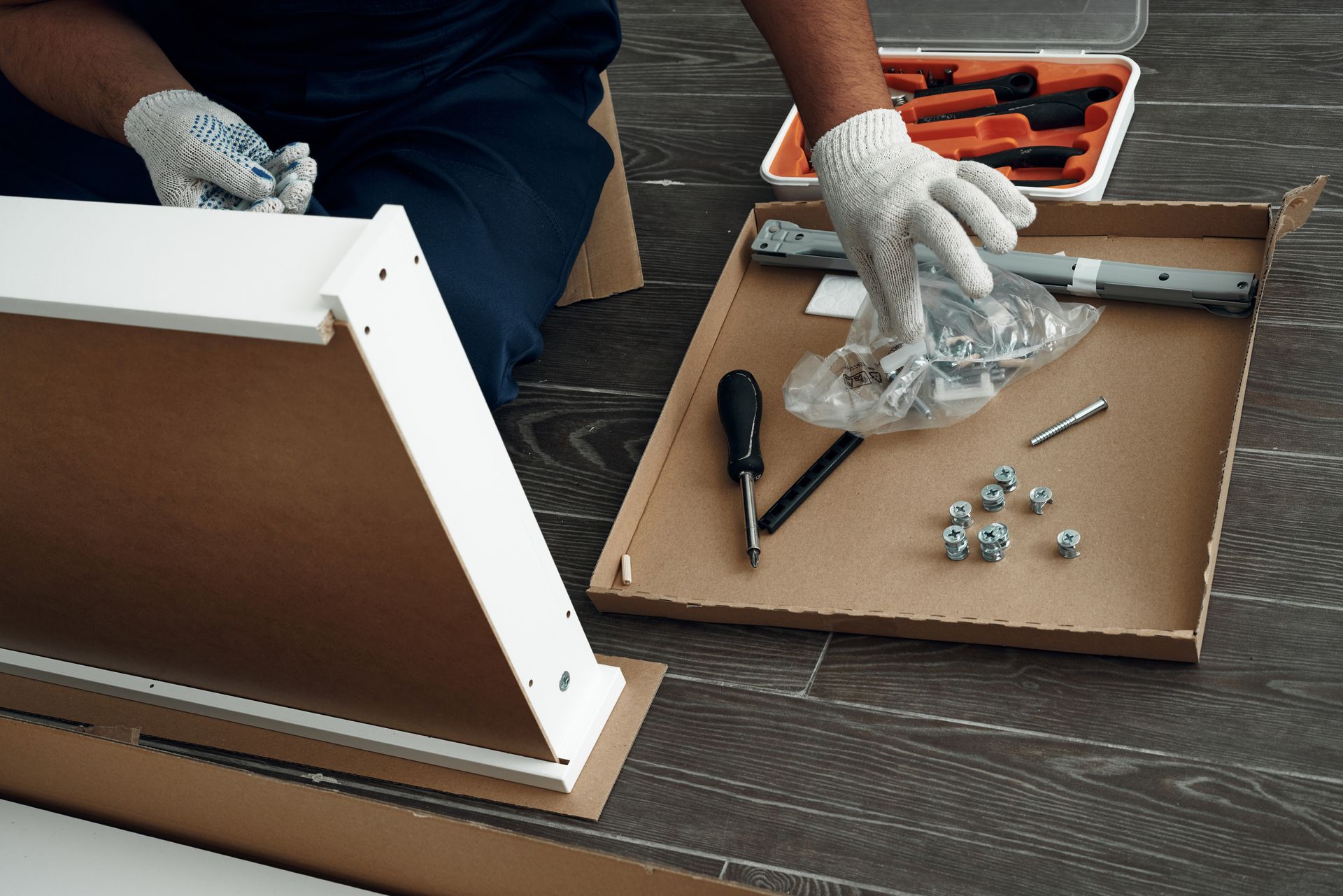 A man is sitting on the floor assembling a piece of furniture.