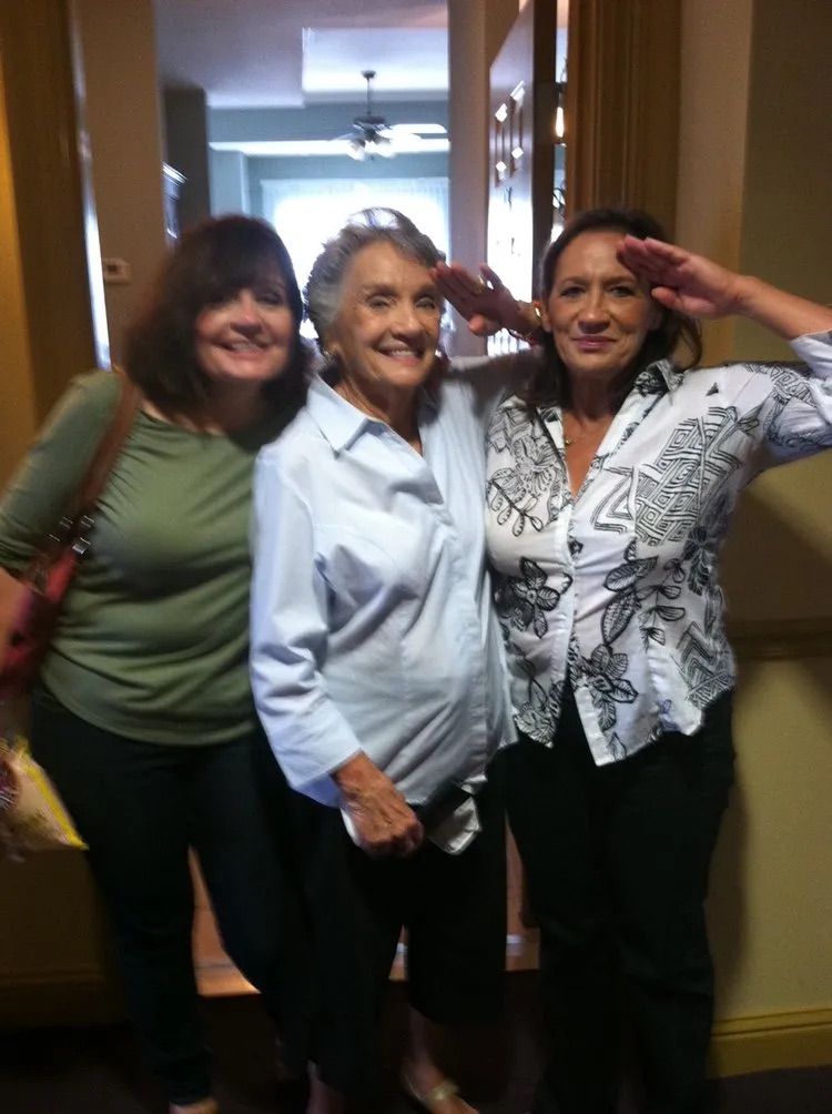 Three people stand in a doorway, smiling at the camera, with one person saluting.