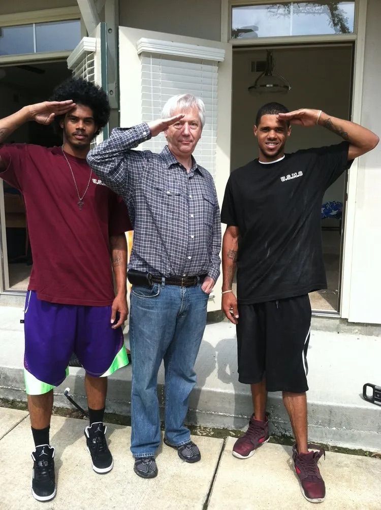Three people stand outdoors, side-by-side, each holding a hand to their forehead in a salute gesture.