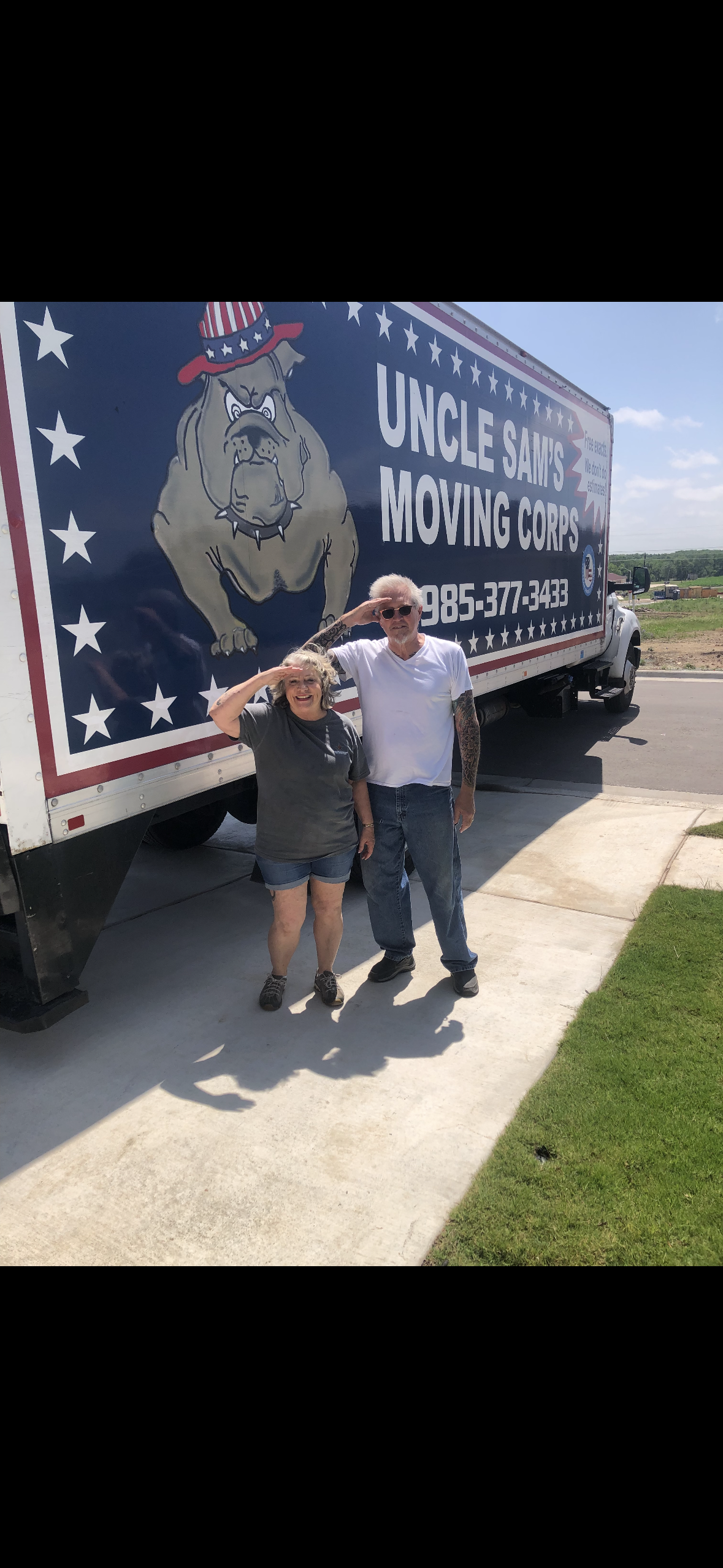 Two people salute in front of a large Uncle Sam’s Moving Company semi-truck decorated with stars and a bulldog logo.