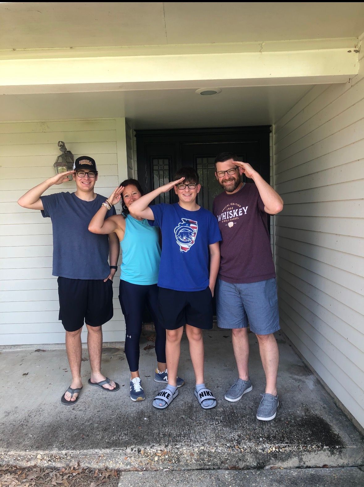 Four people standing under a house entryway, all saluting the camera.