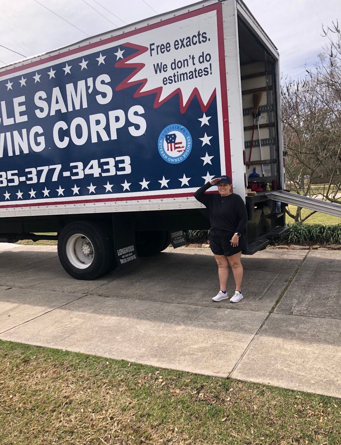 A person in black clothing salutes while standing beside a moving truck labeled 
