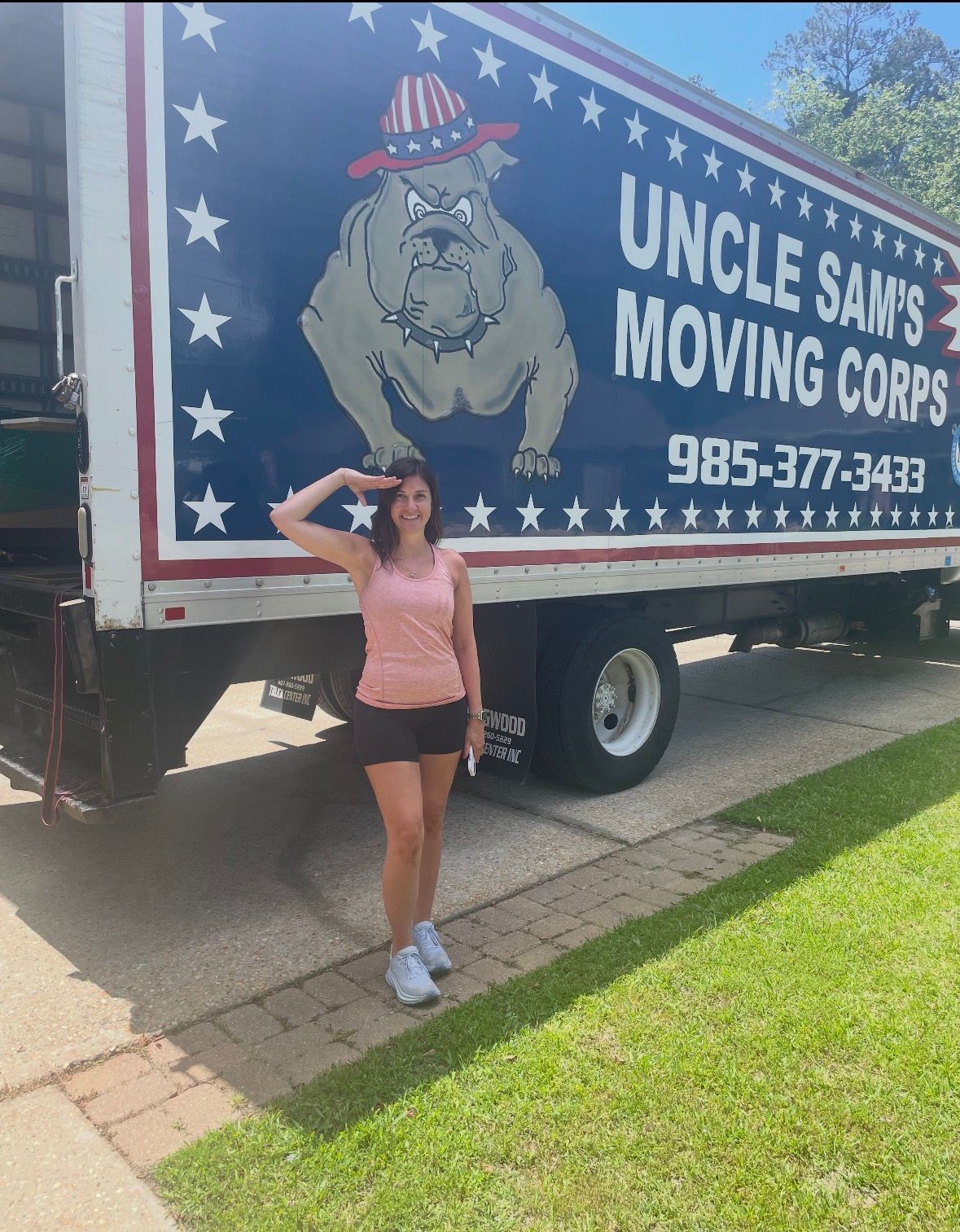 A person stands in front of a blue moving truck branded 