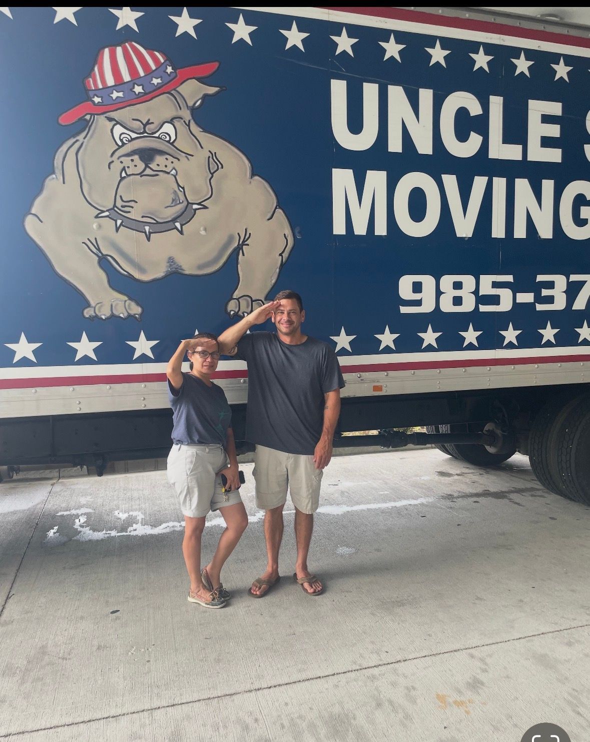Two people saluting in front of a truck with an Uncle Sam-themed bulldog logo and company branding.