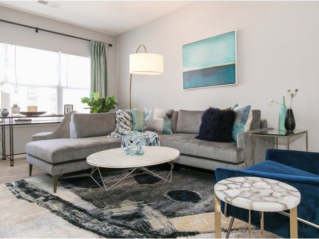 The Village at Odenton Station apartment living room with lamp, sofa, wall art, coffee table, and oversized window.