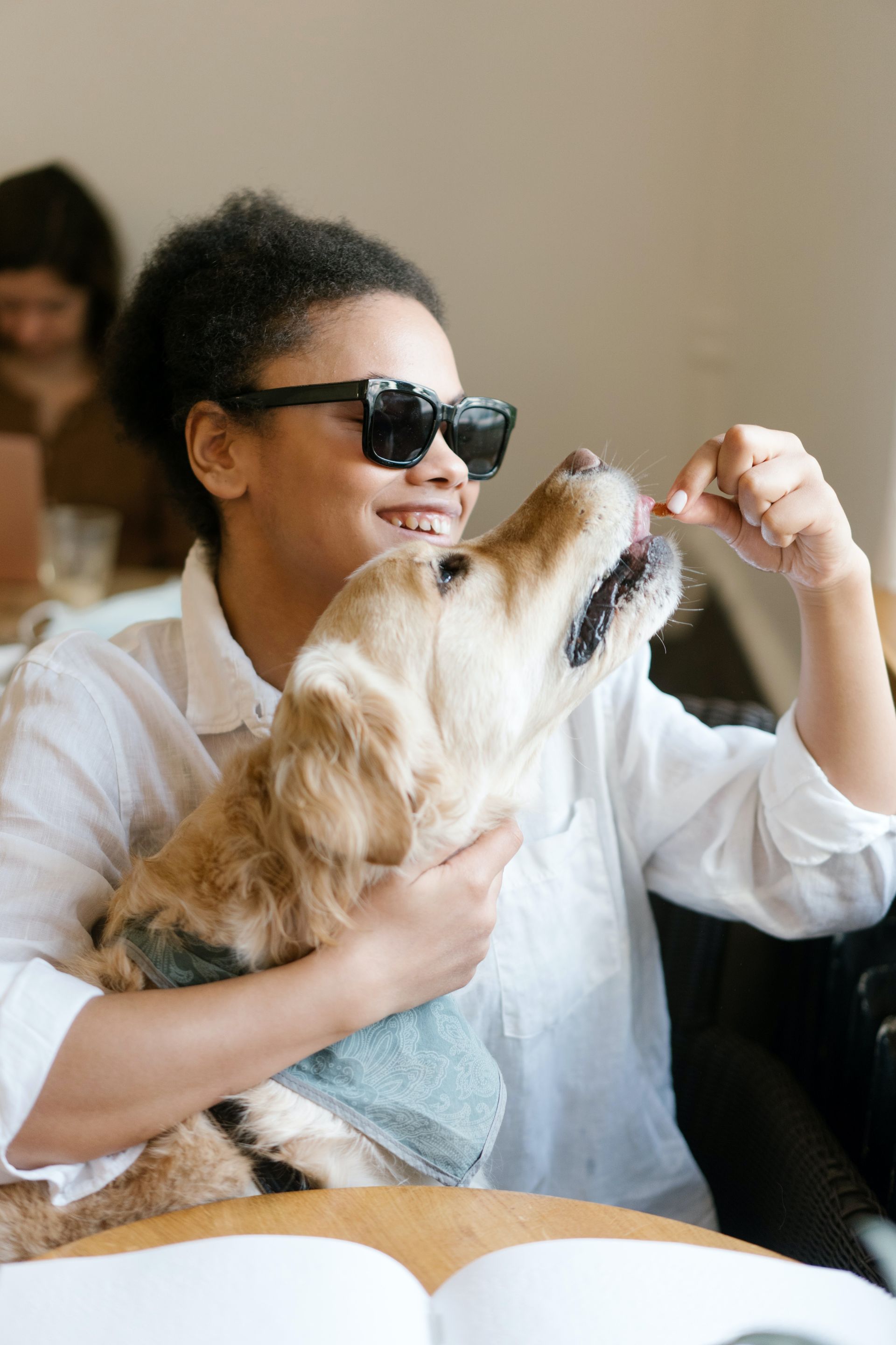 A woman is holding a dog in her arms while sitting at a table.