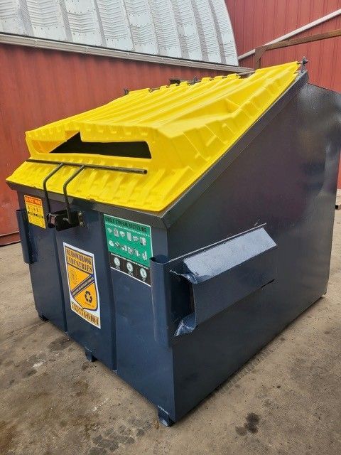 A dark gray industrial waste dumpster with a bright yellow plastic lid, featuring a safety sign on the front.