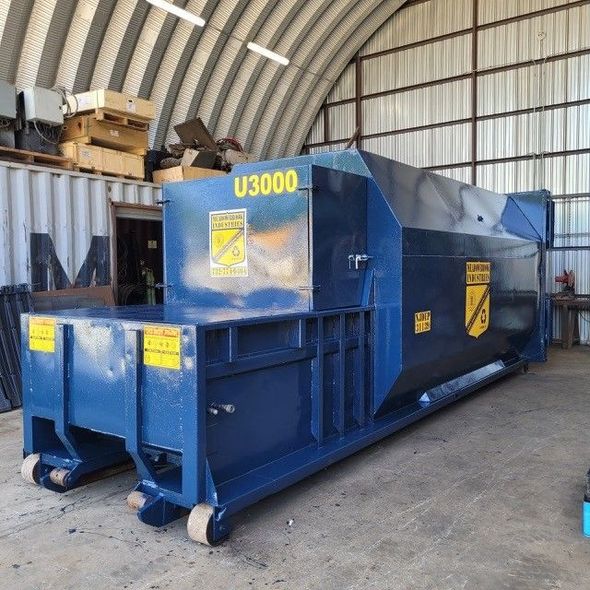 A large blue industrial trash compactor, marked