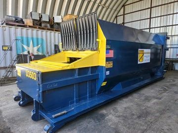 A large industrial blue and yellow trash compactor unit inside a warehouse facility.