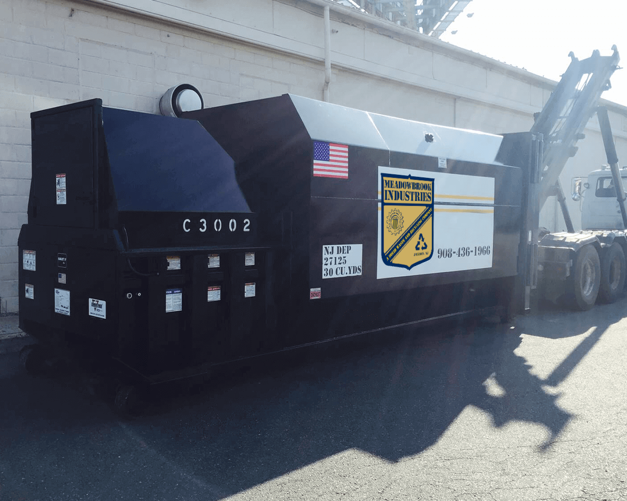 A black and white industrial trash compactor unit with a U.S. flag decal and city seal, parked on a paved outdoor lot.