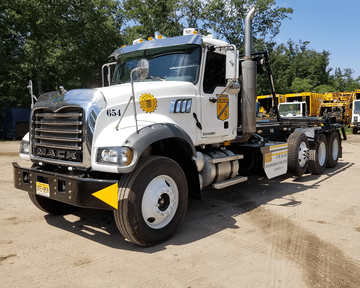 A white Mack roll-off truck parked on a dirt lot with