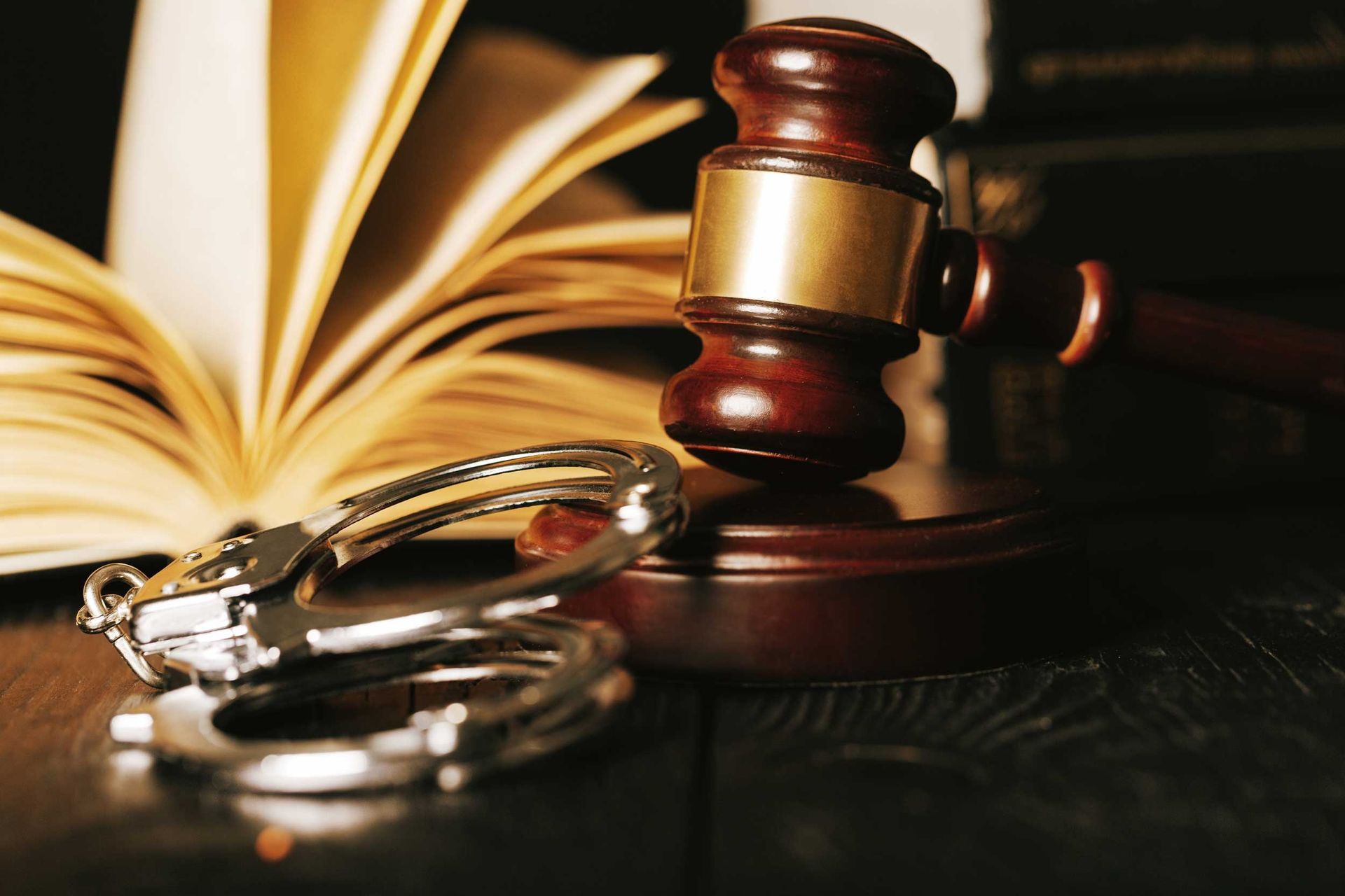 Gavel, handcuffs, and open law book on a dark wooden surface. Gavel, handcuffs, and open law book on a dark wooden surface.