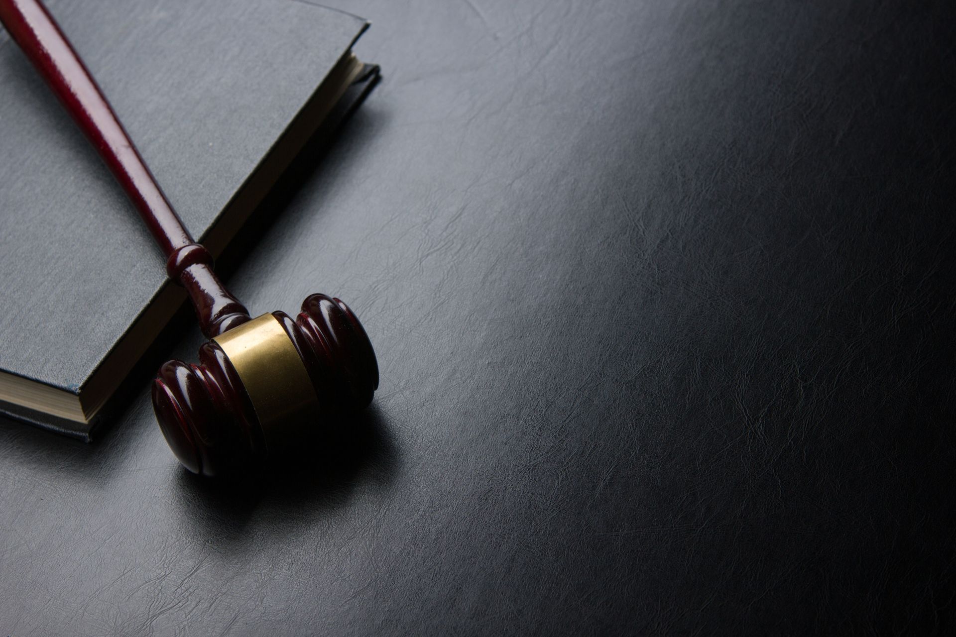 A wooden gavel lies beside a closed law book on a dark desk, symbolizing legal practice.
