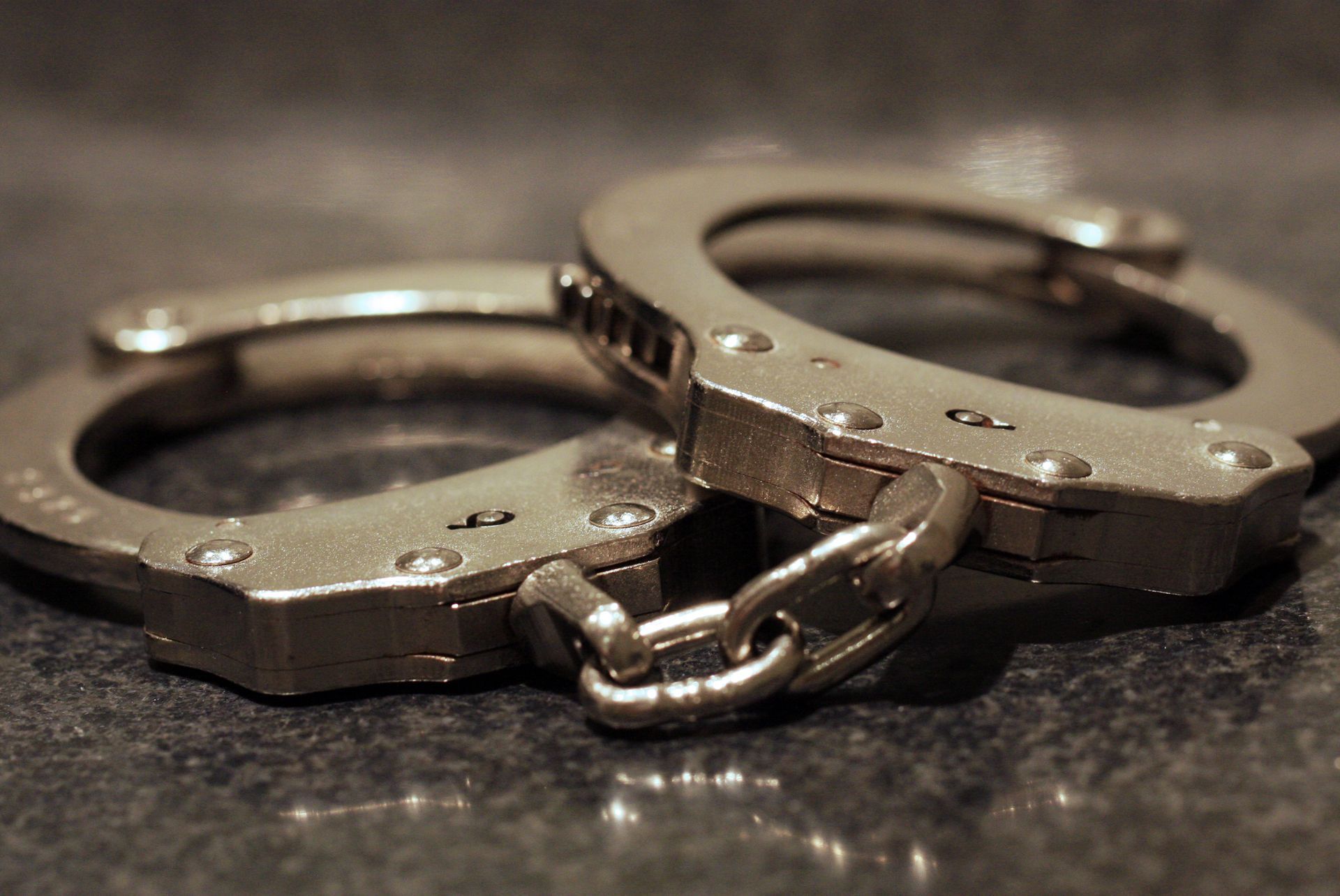 Handcuffs, silver metal, resting on a dark, textured surface.