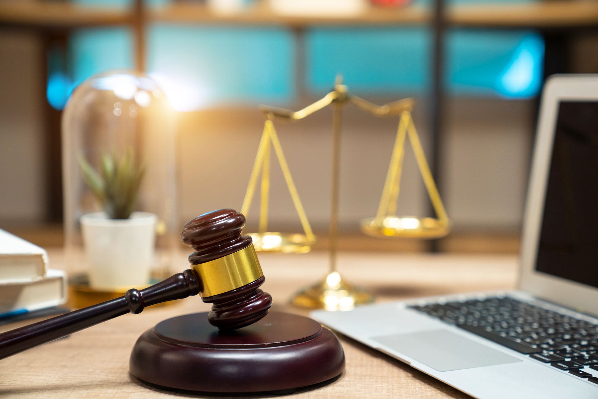 Criminal defense lawyer office desk with gavel, justice scale, laptop, law books, and plant decor.