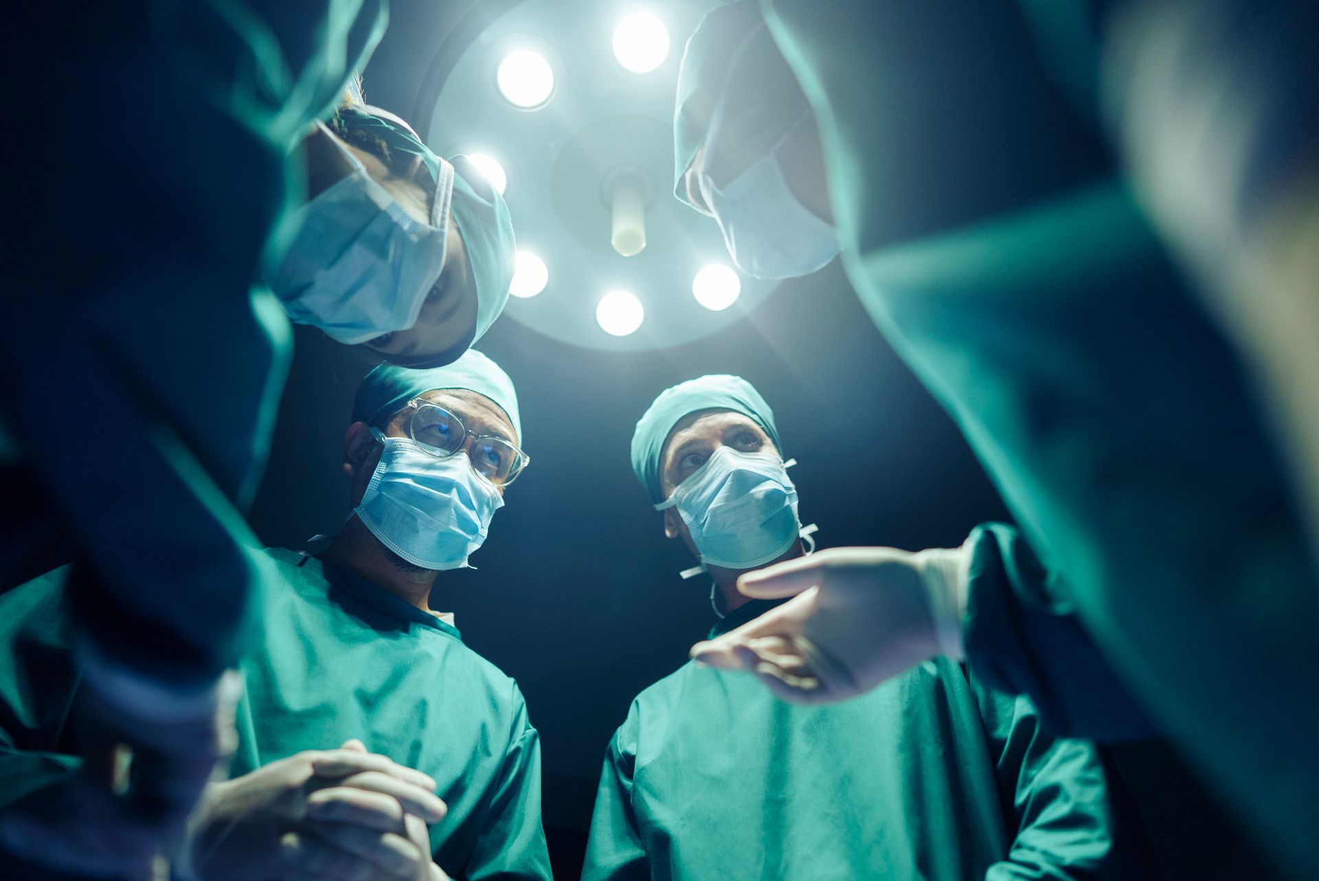 Surgeons in scrubs and masks leaning over a patient under operating room lights.
