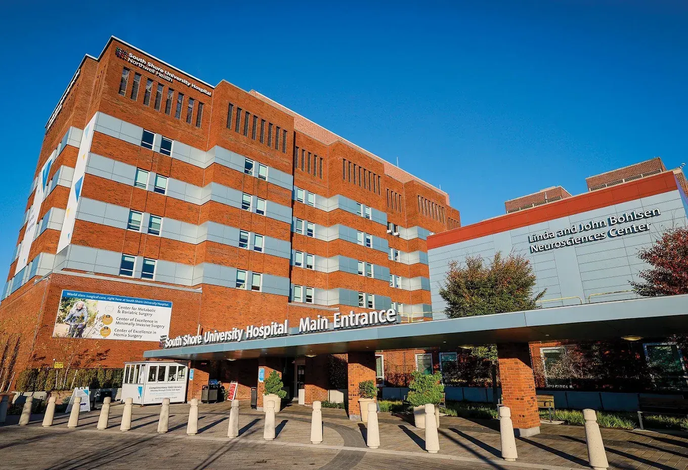 Exterior of a large brick hospital building with a covered entrance under a clear blue sky