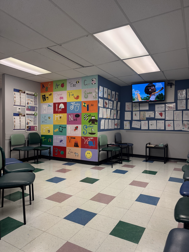 Empty classroom waiting area with colorful wall art, chairs, and a TV mounted on the wall.