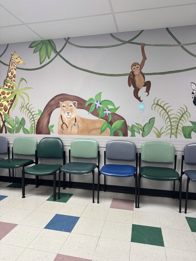 Waiting room with green chairs in front of a jungle mural showing lions, a monkey, and plants.
