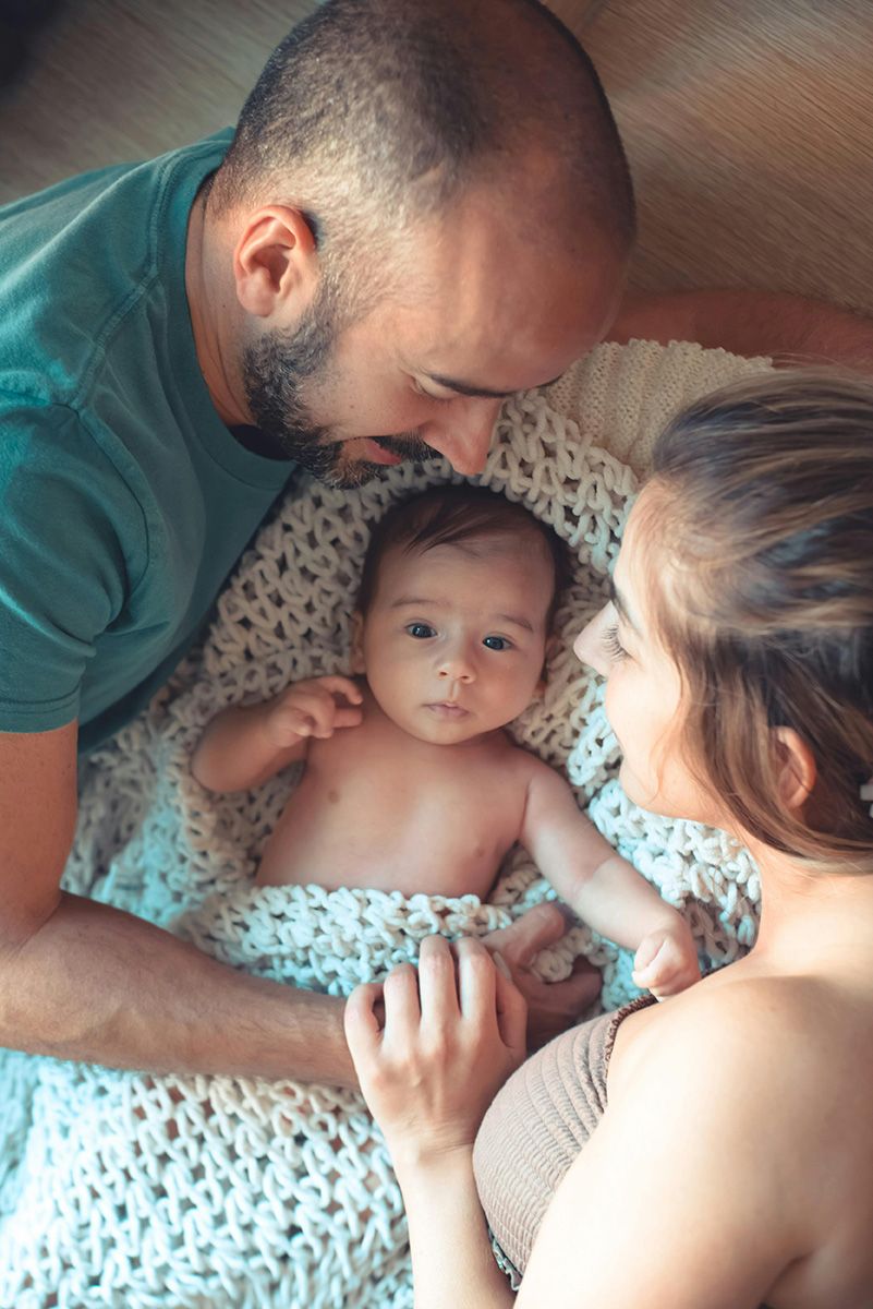 Parents leaning over a baby in a blanket on a couch, looking down affectionately.