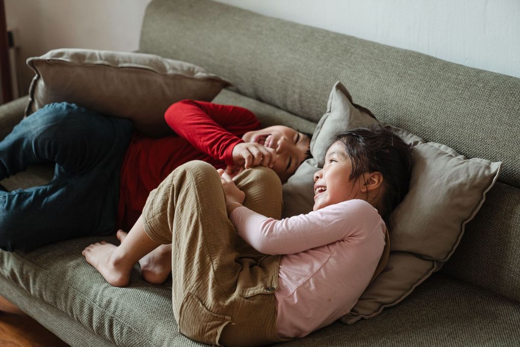 Two people reclining on a couch, smiling and cuddling with pillows and blankets
