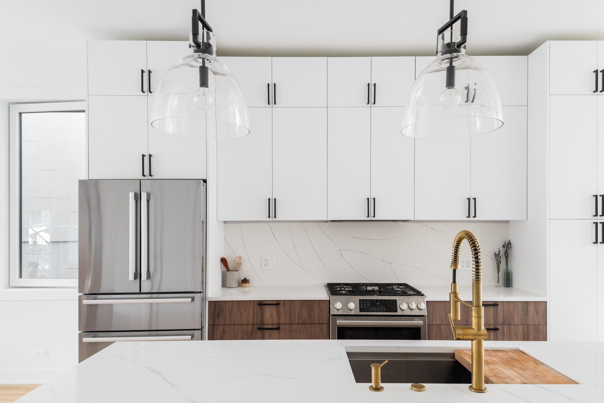 Modern kitchen with white upper cabinets, wood lower cabinets, a stainless steel fridge, and a brass kitchen faucet.