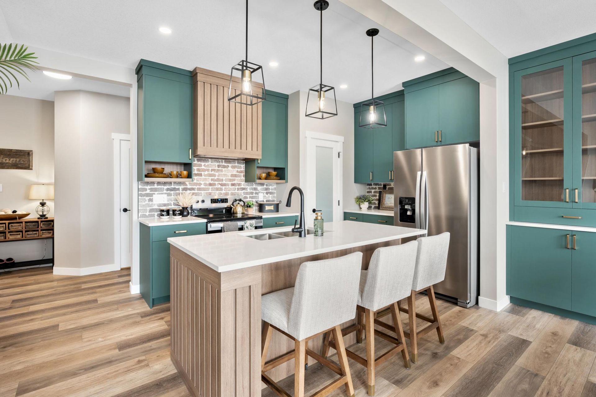 A modern kitchen featuring teal cabinets, a light wood kitchen island with three stools, and stainless steel appliances.