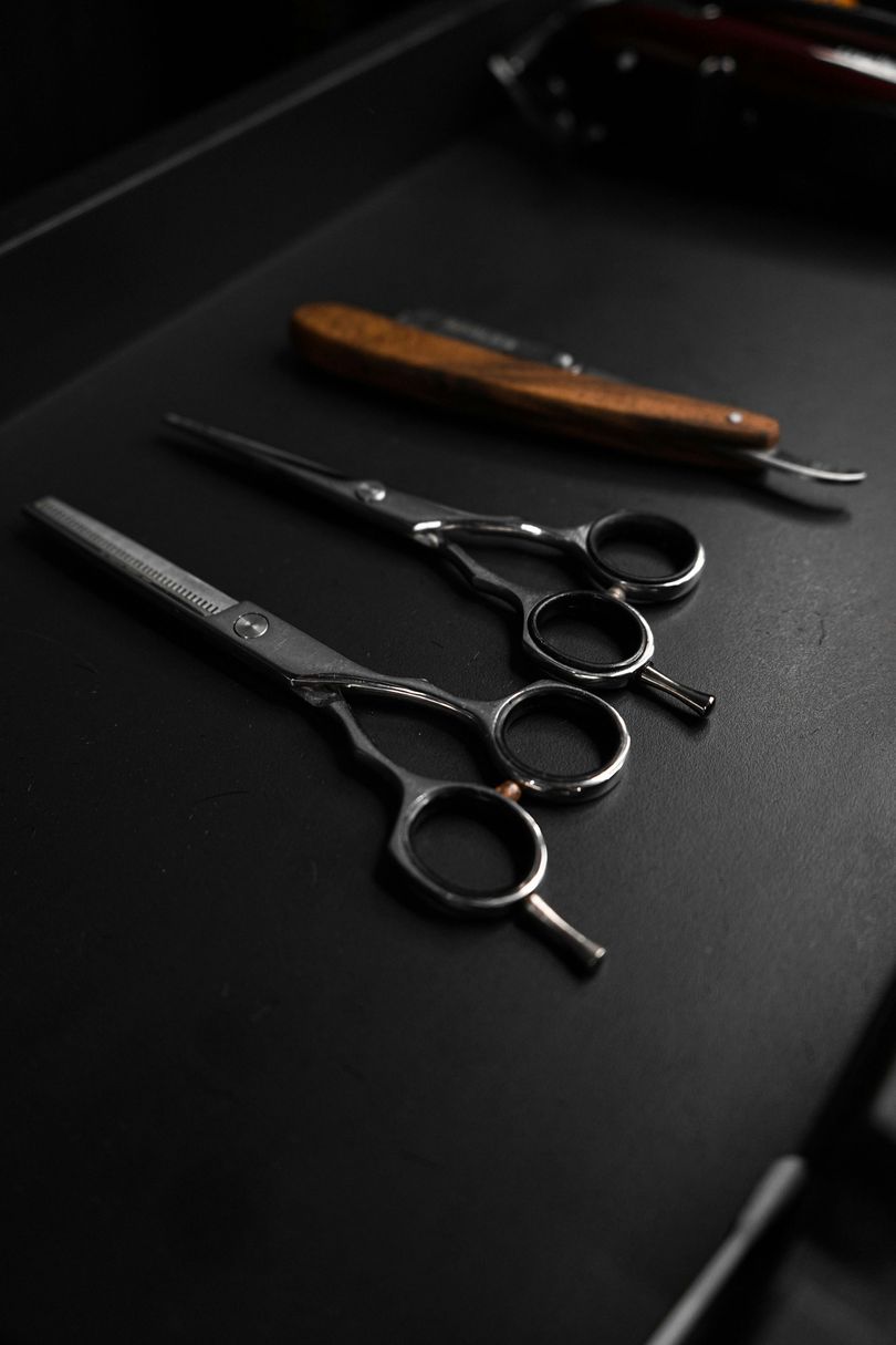 Scissors, straight razor, and clippers on a dark surface, tools of the barber trade.