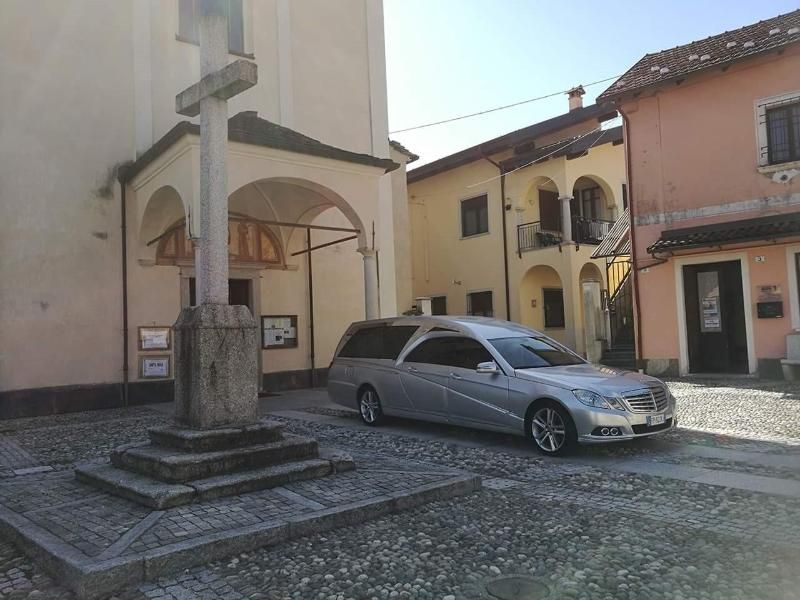 Una berlina argentata parcheggiata in una piazza lastricata, accanto a un monumento in pietra e ad alcuni edifici.