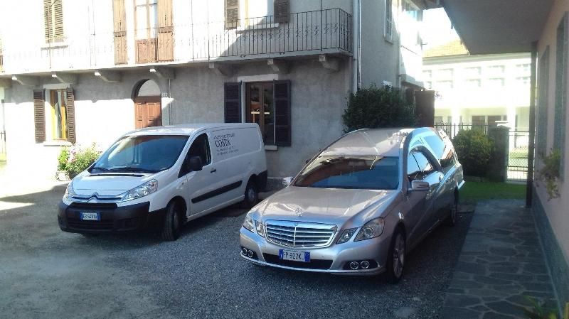 Un furgone bianco e una berlina argento parcheggiati in un cortile pavimentato accanto a un edificio