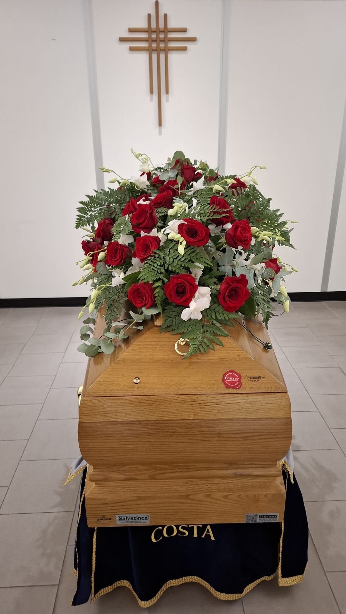 Composizione floreale di fiori rossi e bianchi su una bara di legno in una cappella.