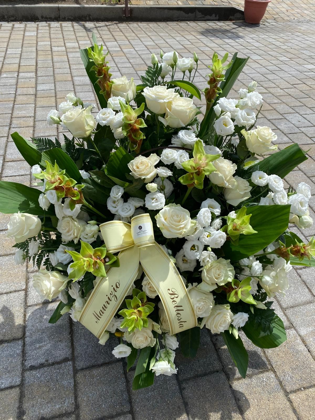 Ghirlanda floreale bianca e verde con nastro su una superficie esterna pavimentata.
