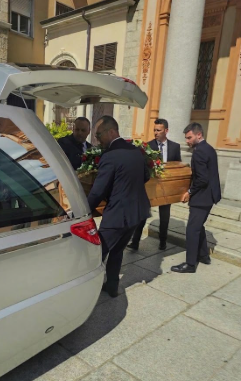 Uomini trasportano una bara da un carro funebre all'ingresso di un edificio.