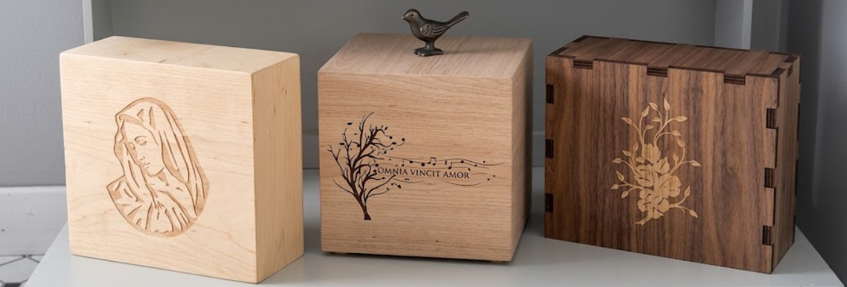 Tre scatole di legno incise, in legno chiaro e scuro, esposte una accanto all'altra.