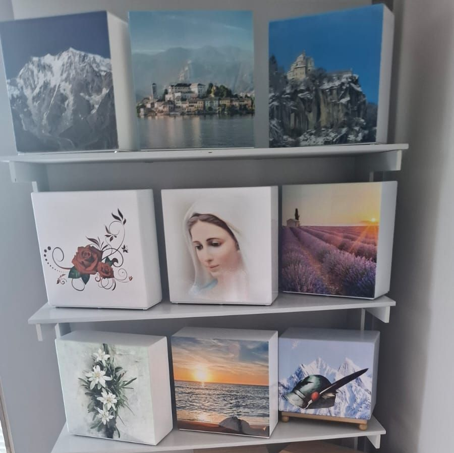 Cubi espositivi per foto su mensole bianche con stampe di paesaggi, ritratti e motivi floreali.