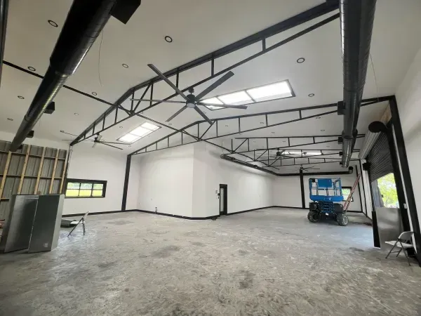 Empty industrial workshop with white walls, exposed ceiling beams, and a blue scissor lift