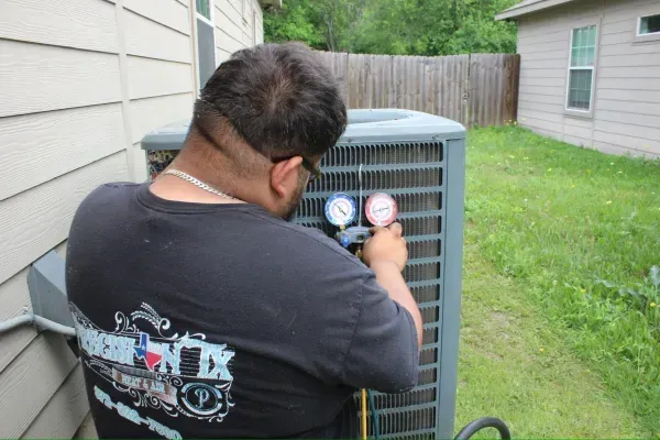 Technician checking air conditioner gauges beside a house in a grassy yard
