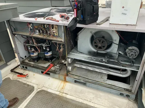 Open HVAC unit with exposed wiring, fan, and coils in a workshop setting.