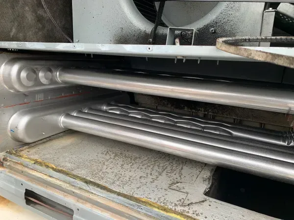 Metal rollers and pipes inside a machine, shown in a tight industrial close-up.