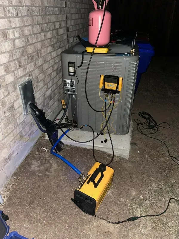 Yellow portable air mover and cords beside a large gray HVAC unit against a brick wall at night