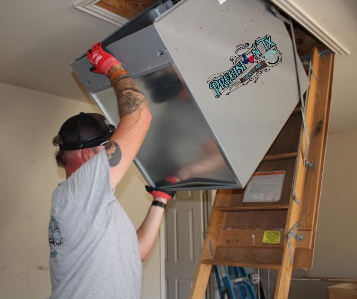 Person lifting a large metal HVAC unit into a ceiling opening with a ladder nearby