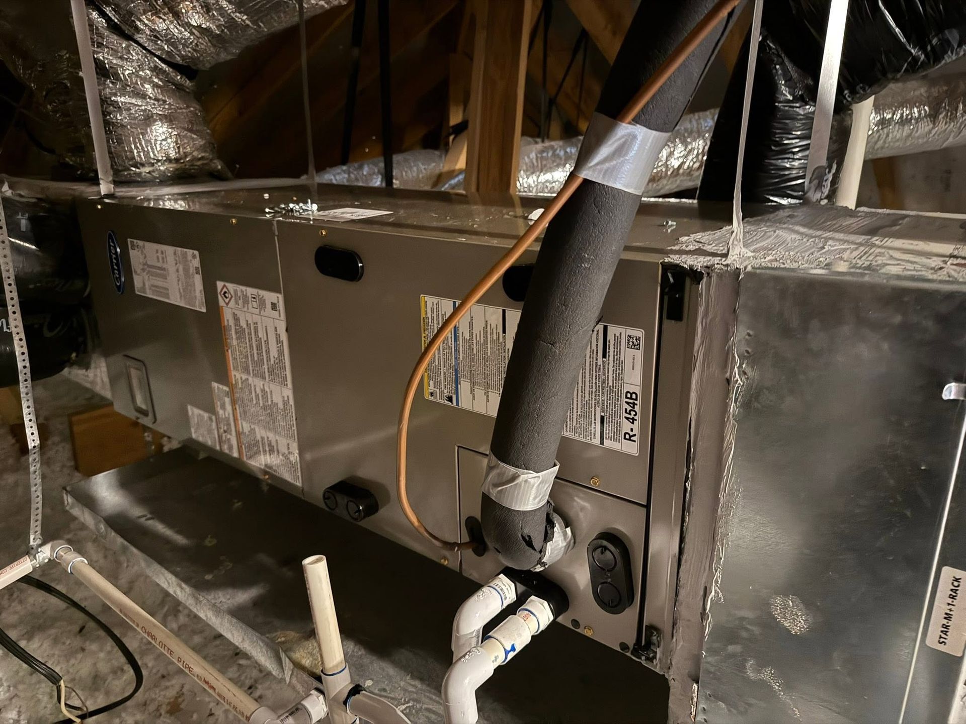 Attic HVAC unit with insulated ducts, wiring, and PVC drain piping