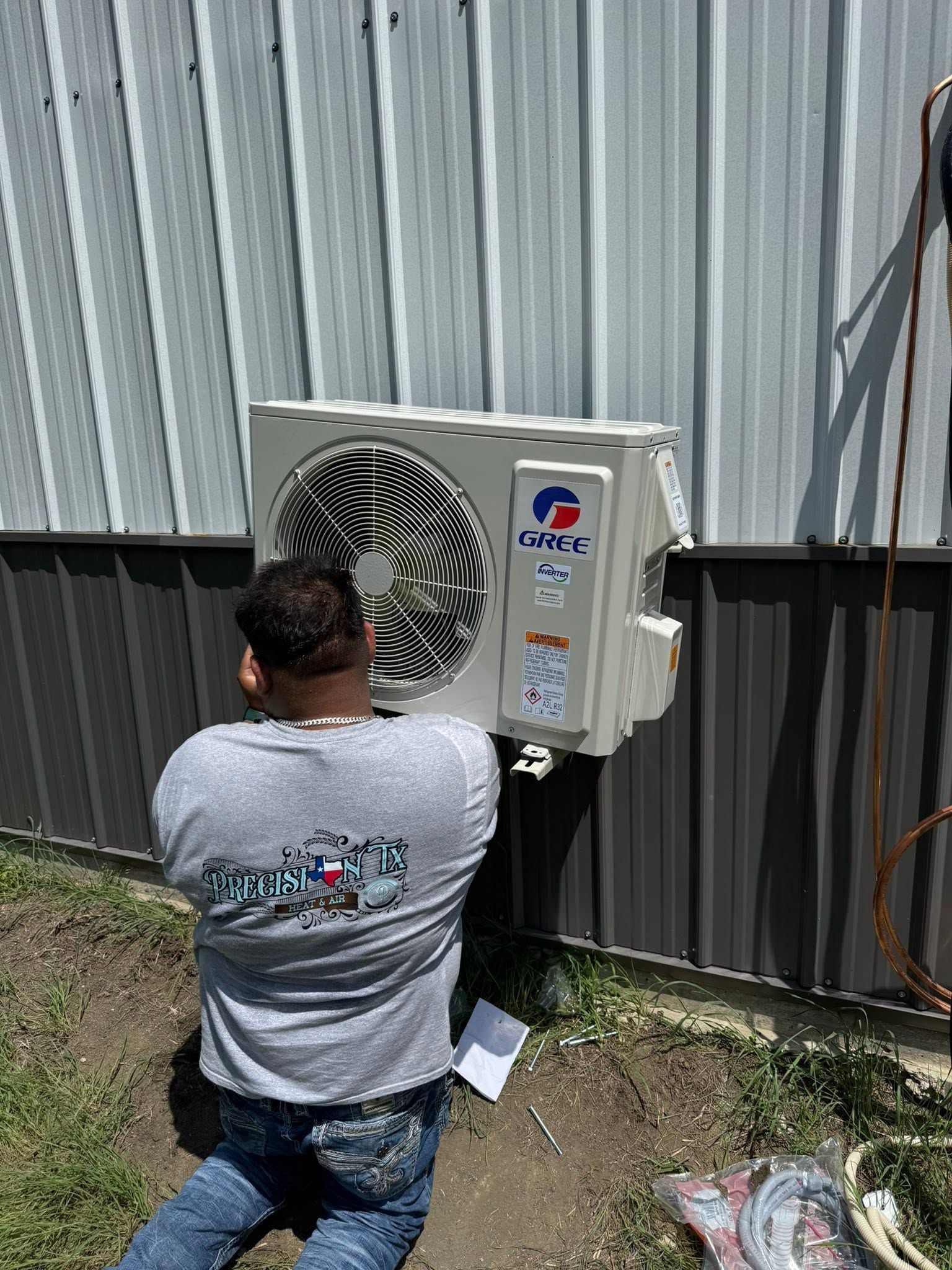 Technician checking gauges on an outdoor air conditioner unit beside a house