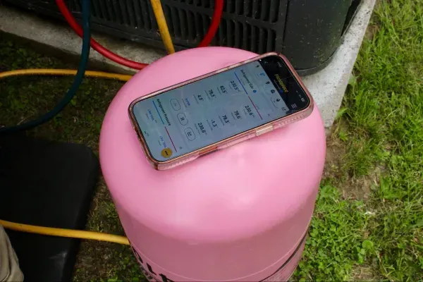 Smartphone resting on a pink stool outdoors near cables and grass.