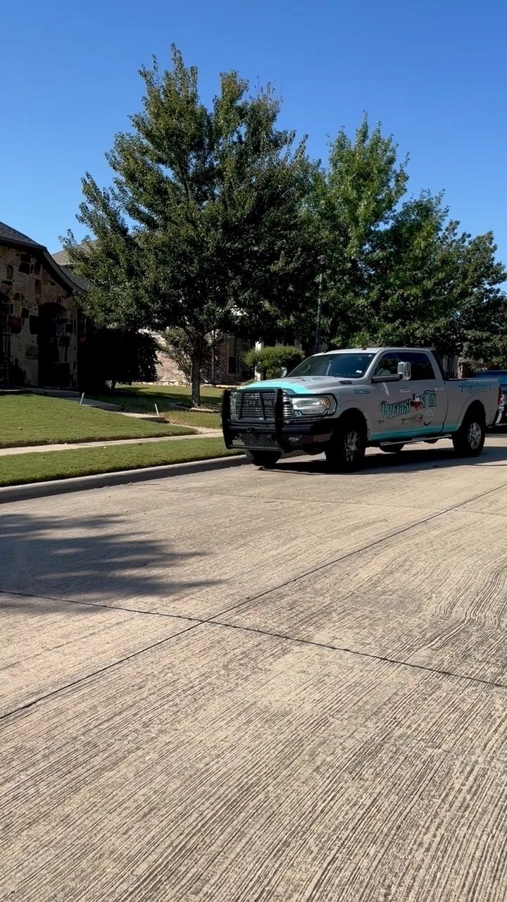 Blue pickup truck parked on a sunny residential street beside a grassy lawn and large tree
